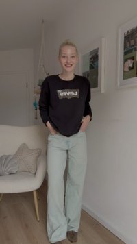 Sweatshirt preto com o logo da Levi's, combinado com calças largas de tom verde claro. A textura é casual, com um ajuste confortável e tons neutros.
