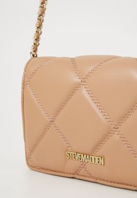 Tan quilted leather crossbody bag with gold chain strap and gold Steve Madden logo plaque on front.