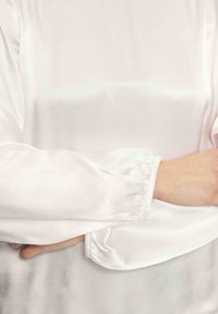 Biała satynowa bluzka z długimi, marszczonymi rękawami oraz gładką, błyszczącą teksturą. Materiał elegancko się układa z minimalnymi detalami.