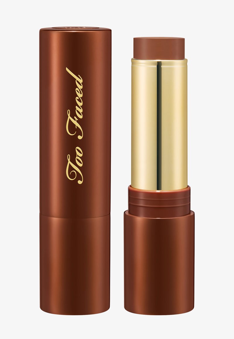Brauner Make-up-Stick mit goldfarbenem Innenrohr, teilweise herausgedreht, neben passendem braunen Deckel mit goldener "Too Faced"-Schrift.