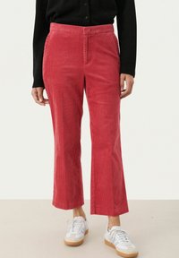 Rode flared corduroy broek met verticale strepen, hoge taille en zijzakken, gecombineerd met witte sneakers en een zwart topje.