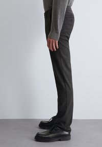 Grijze broek met een subtiele textuur, met een rechte pasvorm, zijzakken en een tailleband. G gedragen met zwarte veterschoenen.