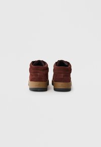 Brown suede high-top sneakers with a textured surface, black lining, and contrasting tan rubber sole featuring embossed branding on the heel.