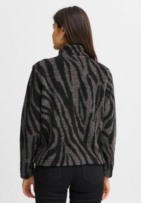 Pull en polaire avec un col montant, présentant un motif zèbre noir et gris. Texture douce, manches longues et coupe légèrement décontractée.