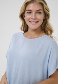 Haut bleu clair à manches courtes en tissu doux et texturé ; présente un col rond et une coupe décontractée. Design simple sans motifs ni accents.