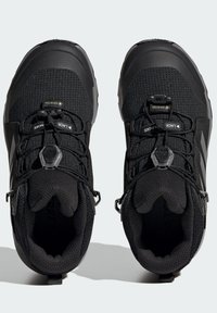 Scarpe da trekking nere con tomaia in tessuto testurizzato, punta in gomma e sistema di lacci integrato. Presentano un colletto imbottito e un'etichetta di estrazione.