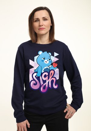 Marineblå sweatshirt med et tegneserieagtigt bjørnegrafik, et æble og ordet "Sigh" i pink og lilla stiliseret skrift.