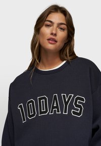 Felpa blu navy con grande scritta bianca "10DAYS", collo rotondo e vestibilità rilassata. Realizzata in tessuto testurizzato con una finitura morbida.