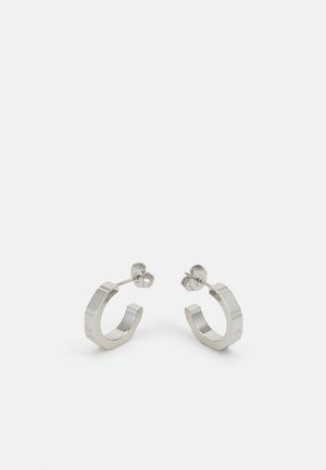 Sølvmetall hoop øredobber med teksturert design, med en liten post bak og merkevare på en hoop. Rund form med polert finish.