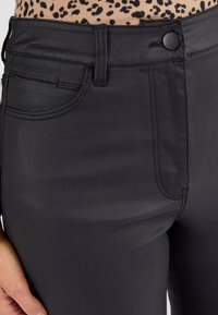 Pantalones de mezclilla negros con una textura suave, que presentan bolsillos frontales, un cierre con botón y un diseño ajustado. La cinturilla es elegante y sin costuras.