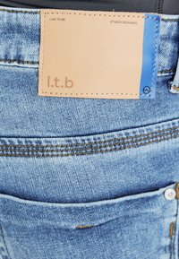 Svijetloplave traperice s kožnom oznakom prošivenom na struku, koja sadrži naziv branda "l.t.b" i kontrastni plavi detalj.