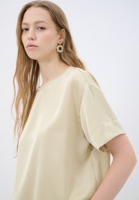 Afslappet fit, cremfaret bluse med korte ærmer, lavet af glat stof. Har en rund udskæring og et simpelt design uden udsmykninger.