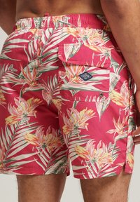 Bañador corto de tejido ligero, con una base rosa y un patrón floral tropical, bolsillo lateral y cintura elástica para mayor comodidad.