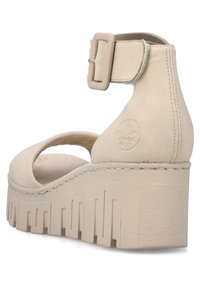 Beige platform sandals with ankle strap, smooth material, rounded toe, textured wedge heel, and decorative stitching detail.