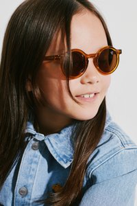 Round, amber-tinted sunglasses with a translucent frame, worn by a child with dark, straight hair and a light blue denim jacket.