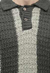 Sötétszürke és krémszínű kötött pulóver texturált mintával, gombos nyakkal és három díszgombbal.