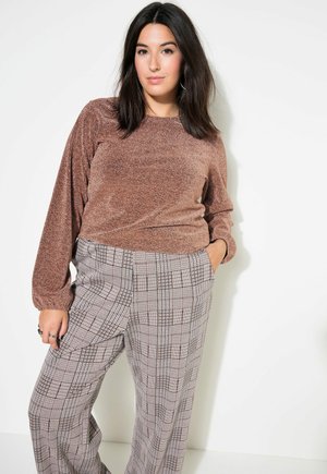 Suéter brillante de bronce de mangas largas combinado con pantalones de pierna ancha en tonos gris y negro a cuadros. Los pantalones presentan una cintura alta y bolsillos laterales.