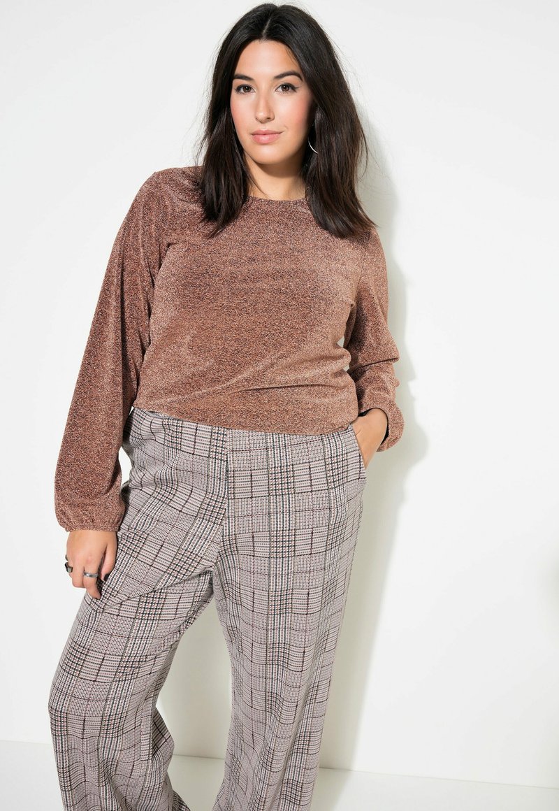 Ein bronzefarbener, glitzernder Pullover mit langen Ärmeln, kombiniert mit weit geschnittenen, grau-schwarz karierten Hosen. Die Hose hat eine hohe Taille und Seitentaschen.