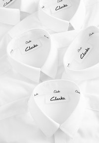Weiße Hemden mit klassischen Kragen, die im Nacken schwarze "Clarks"-Labels tragen. Der Stoff ist glatt und gleichmäßig strukturiert.