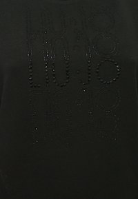 Schwarzes T-Shirt mit strukturierten Strassstein-Details in einem stilisierten Muster, Rundhalsausschnitt und kurzen Ärmeln.