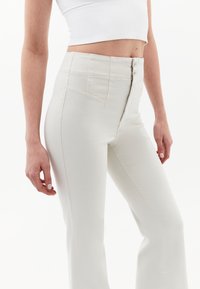 Vita, högmidjade utsvängda jeans gjorda av en strukturerad bomullsmix. Har knappstängning fram och snedställda fickor på höfterna.