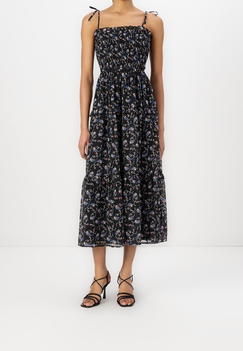Robe maxi noire à fleurs avec corsage smocké, bretelles réglables et jupe à volants. Présente des motifs floraux vibrants en bleu et rouge.