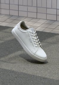 Weiße Ledersneaker mit strukturiertem Obermaterial, runder Zehenpartie und sechs Ösen-Schnürung. Verfügt über eine flache Gummisohle und minimale Markenkennzeichnung.
