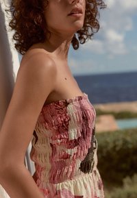 Trägerloses, gerafftes Kleid in Rosa und Creme mit floralem Muster. Leichter Stoff, strukturierte Oberfläche, taillierte Passform, ausgestellter Rock.