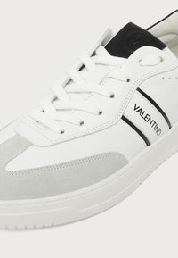 Baskets blanches et grises Valentino avec lacets blancs, accent noir sur la languette et logo Valentino sur le côté.