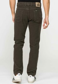Pantaloni dritti marrone scuro in cotone, con un'etichetta del marchio sulla cintura e due tasche posteriori. Indossati con sneakers bianche.
