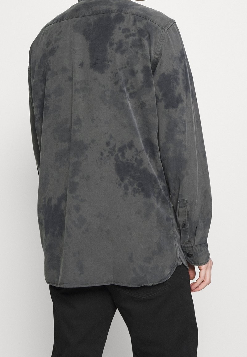 Camicia a maniche lunghe di colore grigio scuro con motivo tie-dye, realizzata in tessuto morbido. Presenta un colletto classico e polsini con bottoni. I bordi sono leggermente curvati.