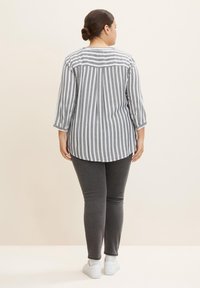 Blusa a rayas en gris y blanco, con un dobladillo redondeado y mangas de tres cuartos, combinada con pantalones ajustados gris oscuro y zapatillas blancas.