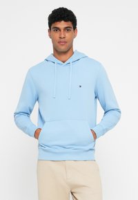 Ανοιχτό μπλε φούτερ από μαλακό ύφασμα, με ρυθμιζόμενη κουκούλα με κορδόνι, μπροστινή τσέπη και μικρό λογότυπο στο στήθος.