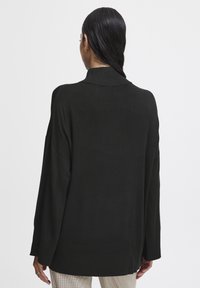 Pulover negru supradimensionat cu un guler înalt, cu nervuri, mâneci lungi și o textură netedă, asortat cu pantaloni cu carouri.