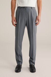 Mężczyzna w szarych spodniach w prążki i czarnych skórzanych mokasynach, stojący z rękami swobodnie opuszczonymi wzdłuż ciała na neutralnym tle.