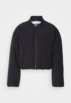 Juoda trumpa bombonešio striukė, lygi medžiaga, užtrauktukas priekyje, du užtrauktukais užsegami šoniniai kišenės, ribuotas apačios kraštas, be matomų raštų ar papuošimų.