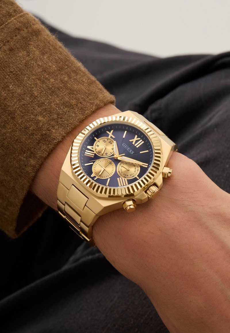 Montre chronographe dorée avec un cadran bleu foncé, de grands index horaires et un bracelet en acier inoxydable avec une finition texturée.
