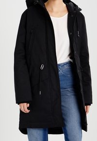 Zwarte parka jack met een capuchon, ritssluiting aan de voorkant, verstelbare trekkoord taille en zijzakken, gemaakt van een gestructureerde, waterafstotende stof.