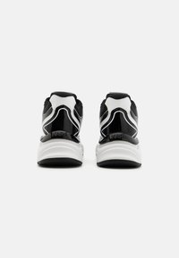Baskets noires et blanches avec un dessus en maille texturée, des accents en vernis brillant et une semelle blanche rembourrée. Logo au niveau du talon.
