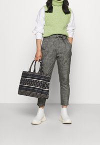 Texturerad grön ärmlös tröja, vit skjorta under, grå rutiga byxor och en mönstrad marinblå tote-väska. Vita ankelstövlar.