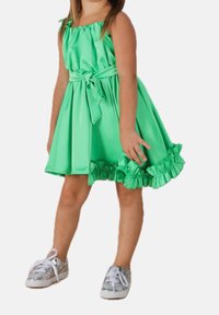 Zielona sukienka z satyny z falbaną u dołu, regulowanym gorsetowym topem i przewiązaną w pasie szarfą. W zestawie z srebrnymi trampkami.