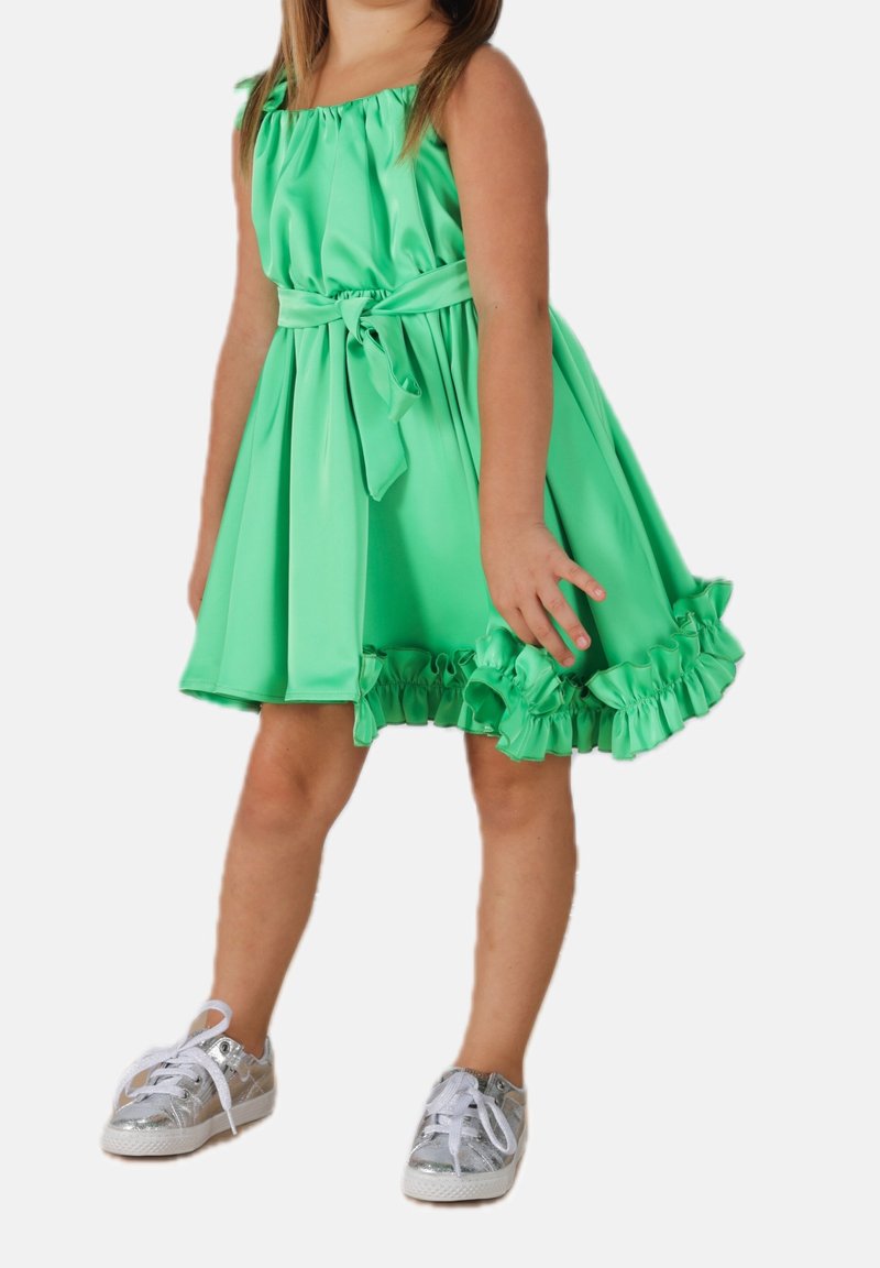 Zielona sukienka z satyny z falbaną u dołu, regulowanym gorsetowym topem i przewiązaną w pasie szarfą. W zestawie z srebrnymi trampkami.