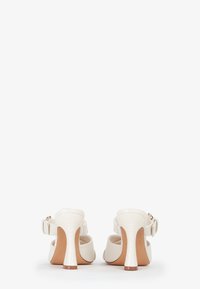 Witte hakken met een gestructureerde afwerking, voorzien van een ronde neus, een slingback band en een taps toelopende hak met een bruine ondertoon.