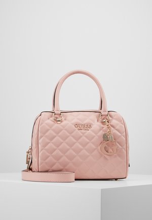 Sac à main matelassé rose avec double poignées et bandoulière amovible, ornée d'un logo et de breloques dorés, présenté sur une surface blanche.