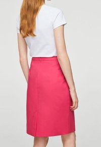 Jupe crayon rose en tissu lisse, dotée d'une fente au dos, d'une silhouette ajustée et d'une taille propre, associée à un haut blanc à manches courtes.