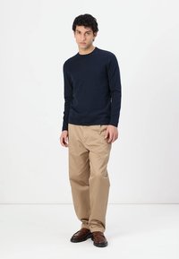 Marineblauses Langarmshirt, kombiniert mit beigen Hosen. Das Shirt hat einen Rundhalsausschnitt, während die Hose einen lockeren Schnitt und ein einfaches Design aufweist. Braune Schuhe runden den Look ab.