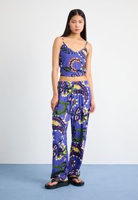 Dvodijelni outfit s ljubičastim cropped topom i širokim hlačama, oboje s šarenim cvjetnim uzorkom. Materijal izgleda lagan i gladak.