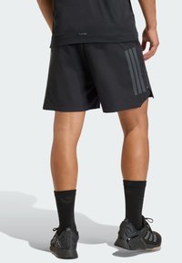 Pantalones cortos atléticos negros con acentos a rayas grises, fabricados con tela ligera. Presentan aberturas laterales para mayor movilidad, combinados con calcetines y zapatos negros.