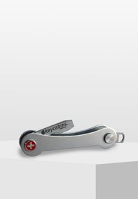 Silver nyckelorganisatör med en schweizisk korslogotyp, som har en slät design och en vridmekanism för enkel tillgång till nycklar.