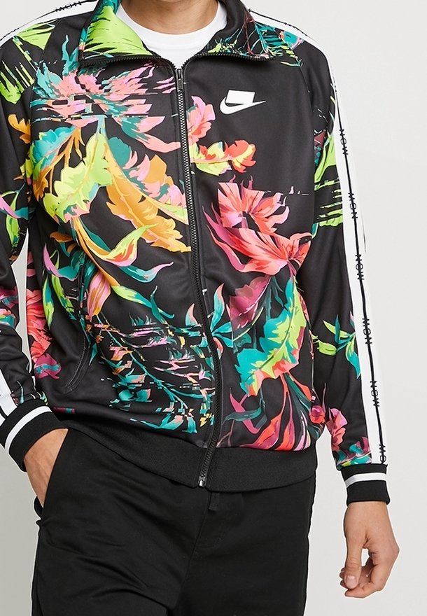 Svart jacka med livfulla blommönster i rosa, gult och grönt. Har dragkedjestängning, vita detaljer och en Nike-logotyp på bröstet.